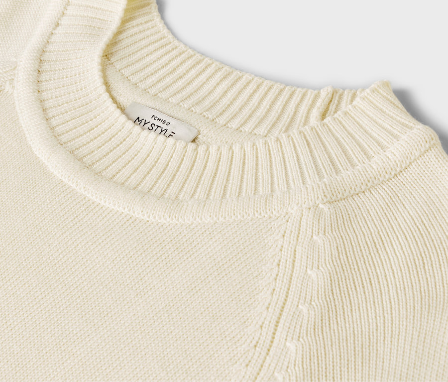 Egy krémszínű, hosszú kötött pulóver részletének közeli képe.