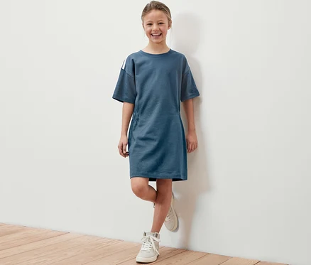Mosolygó lány pózol kék nehéz jersey gyerekruhában, fehér cipővel.