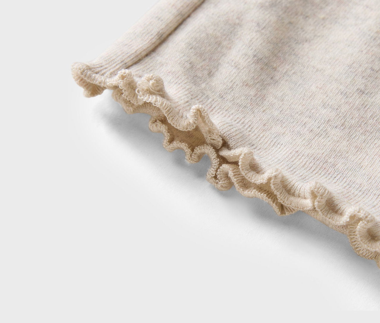 Egy bézs színű pulóver részlete fodros szegéllyel.