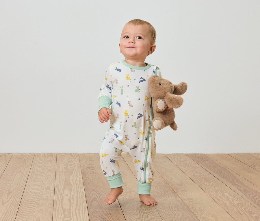 Egy baba áll a fapadlón, és egy plüss elefántot tart.