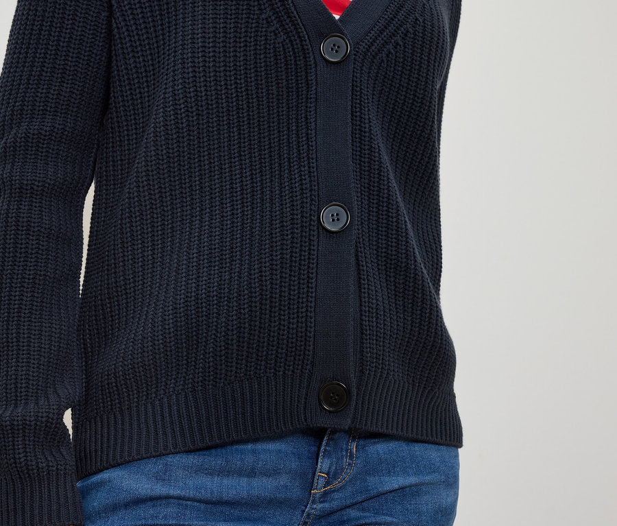 Egy személy törzse sötétkék kötött, gombos kardigánban és kék farmerben.