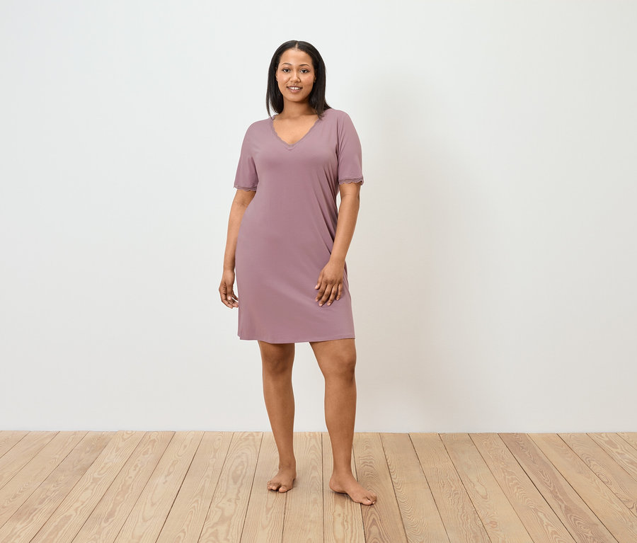 Egy nő áll mezítláb, és egy rövid, mályvaszínű hálóinget visel.