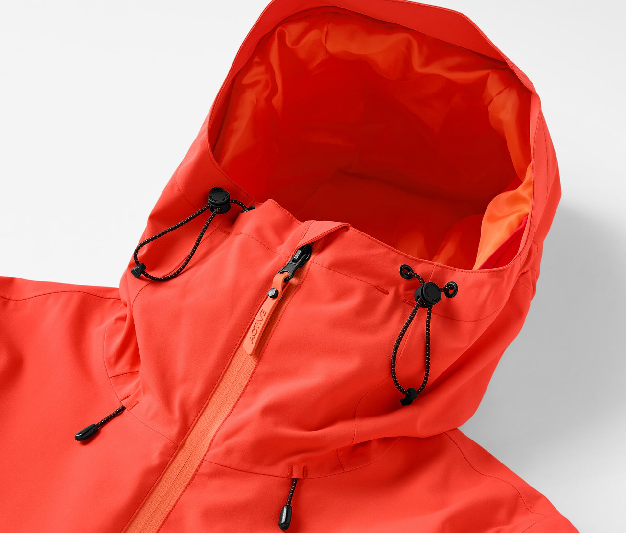 Egy narancssárga kapucnis kabát részlete, húzózsinórral és cipzárral.