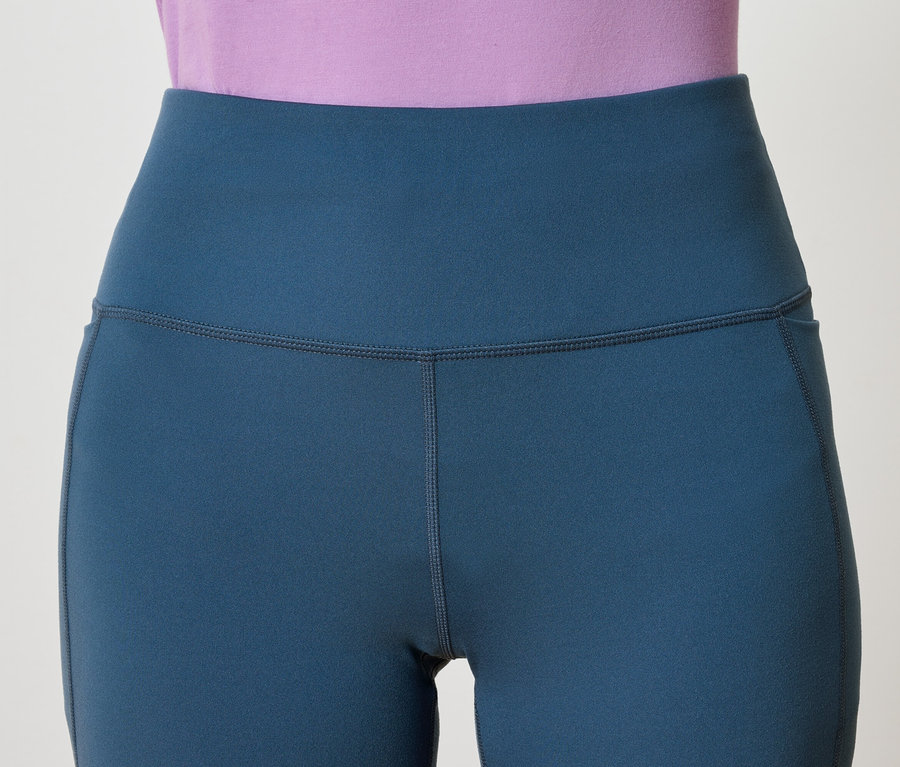 Egy kék, magas derekú leggings részlete egy zsebbel, egy lila felsővel kombinálva.