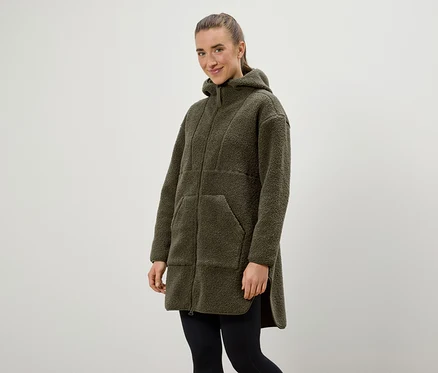 Nő visel olívazöld kapucnis kabátot és fekete leggingset.