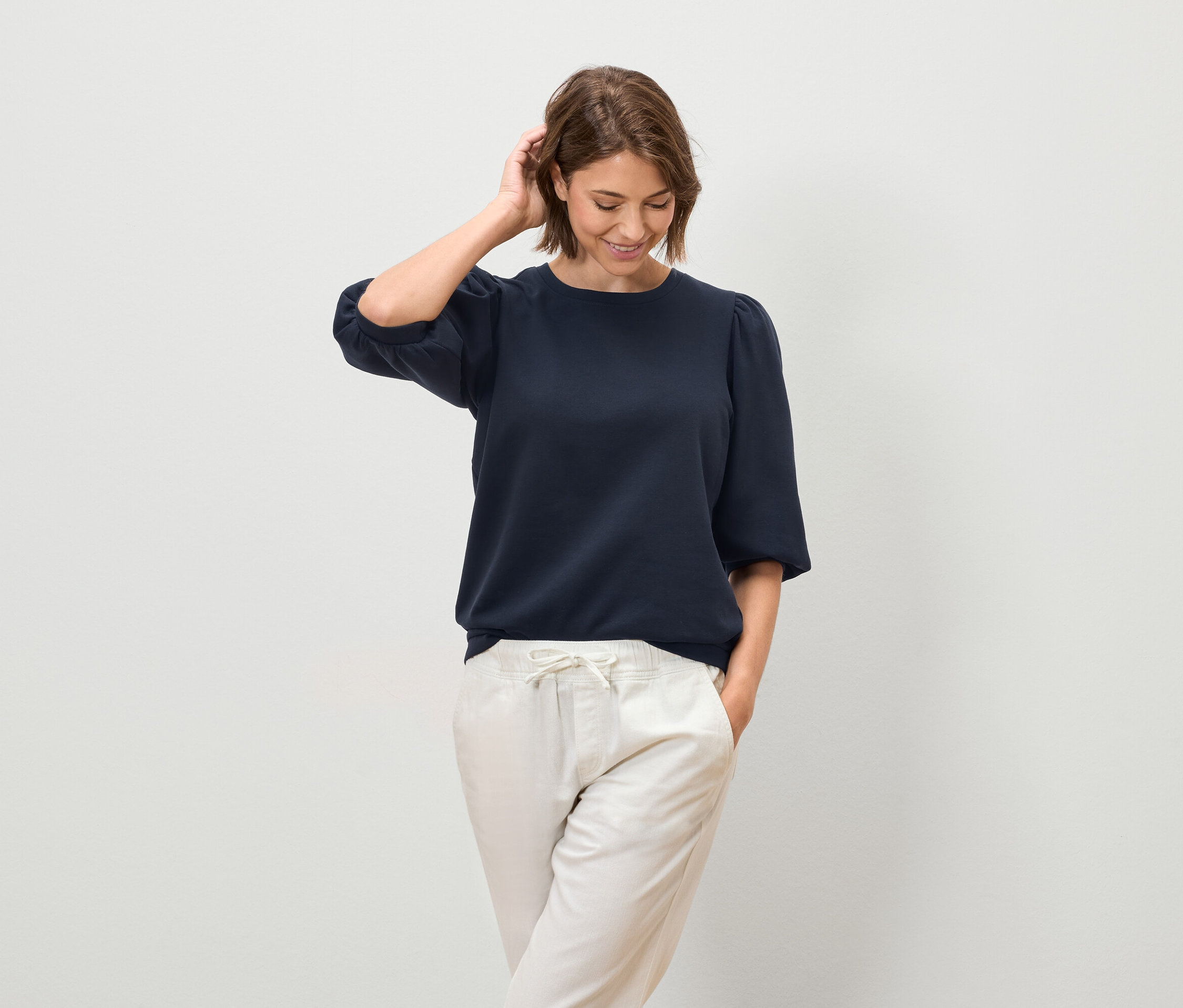 Nő pózol egy rövid ujjú, sötétkék blúzban és világos nadrágban.