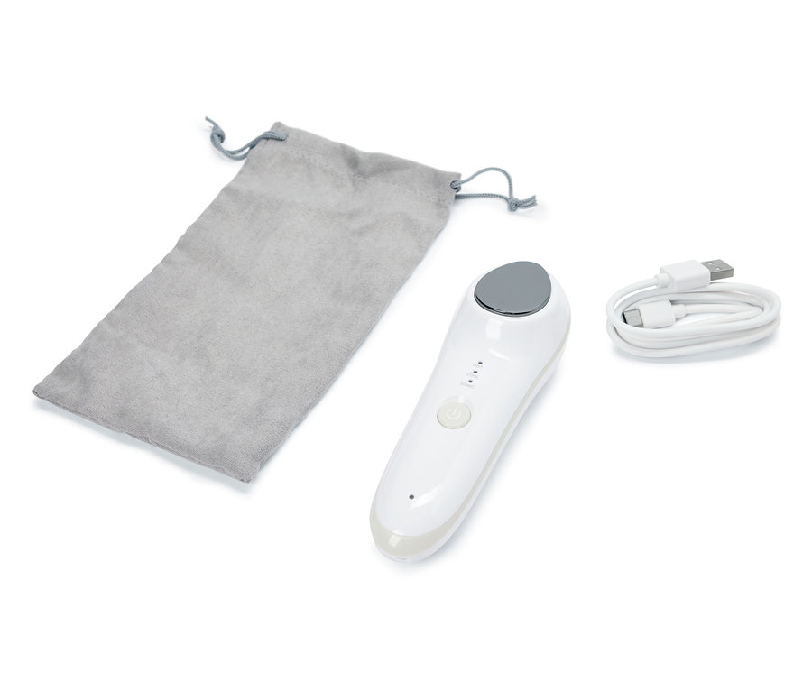 Egy 4 az 1-ben vibrációs arcmasszírozó készülék, egy szürke tasak és egy USB-kábel fekszik fehér alapon.