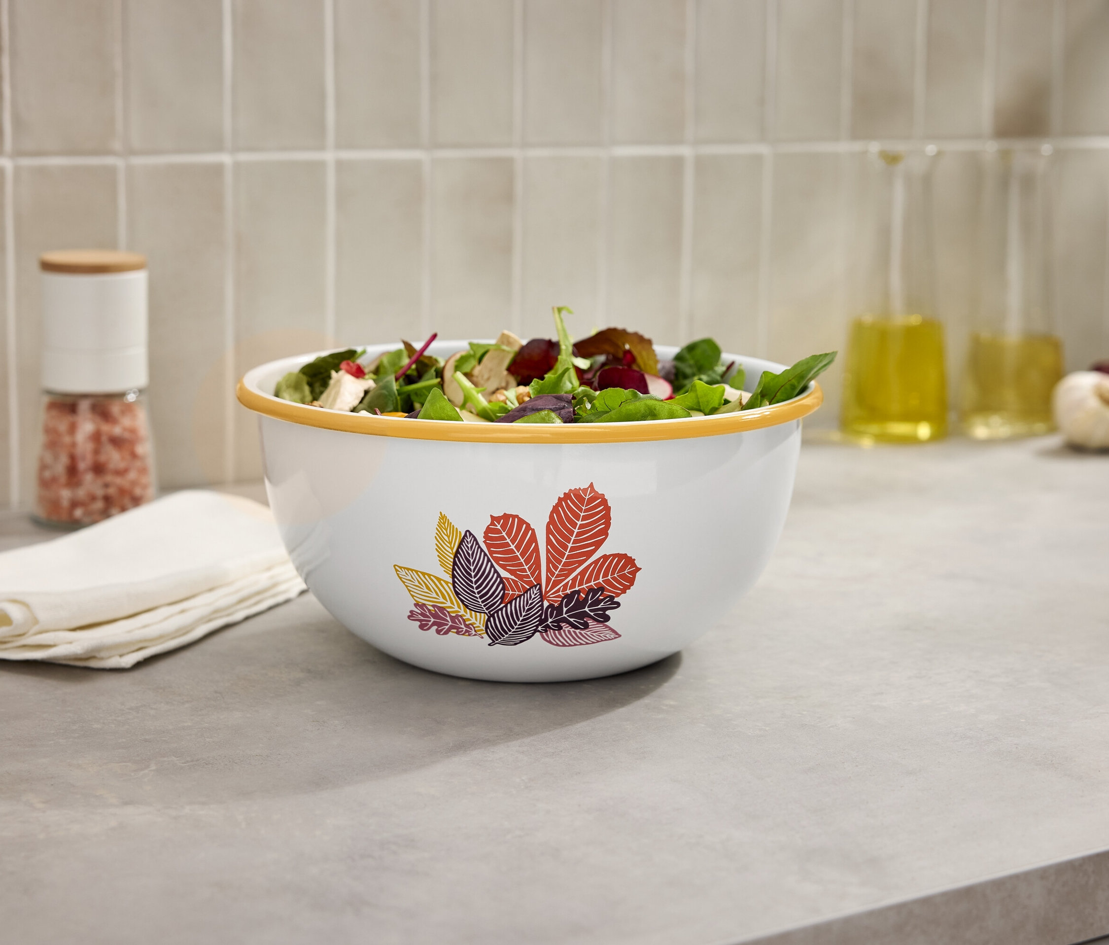 Salátos tál a konyhapulton egy sóőrlő és olajos palackok mellett.