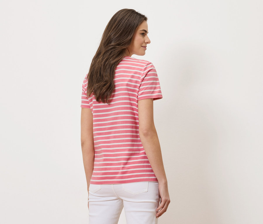 Hátulról látható nő, rózsaszín-fehér csíkos pólót és fehér farmert visel.