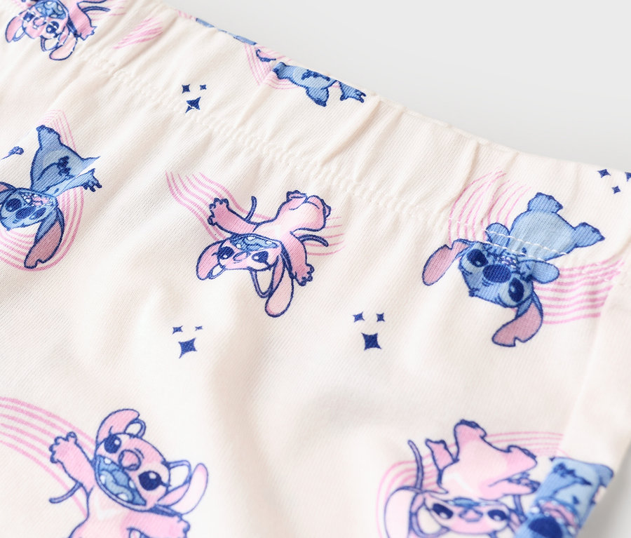 Közeli kép egy bézs színű leggingsről, kék és rózsaszín Stitch mintával.