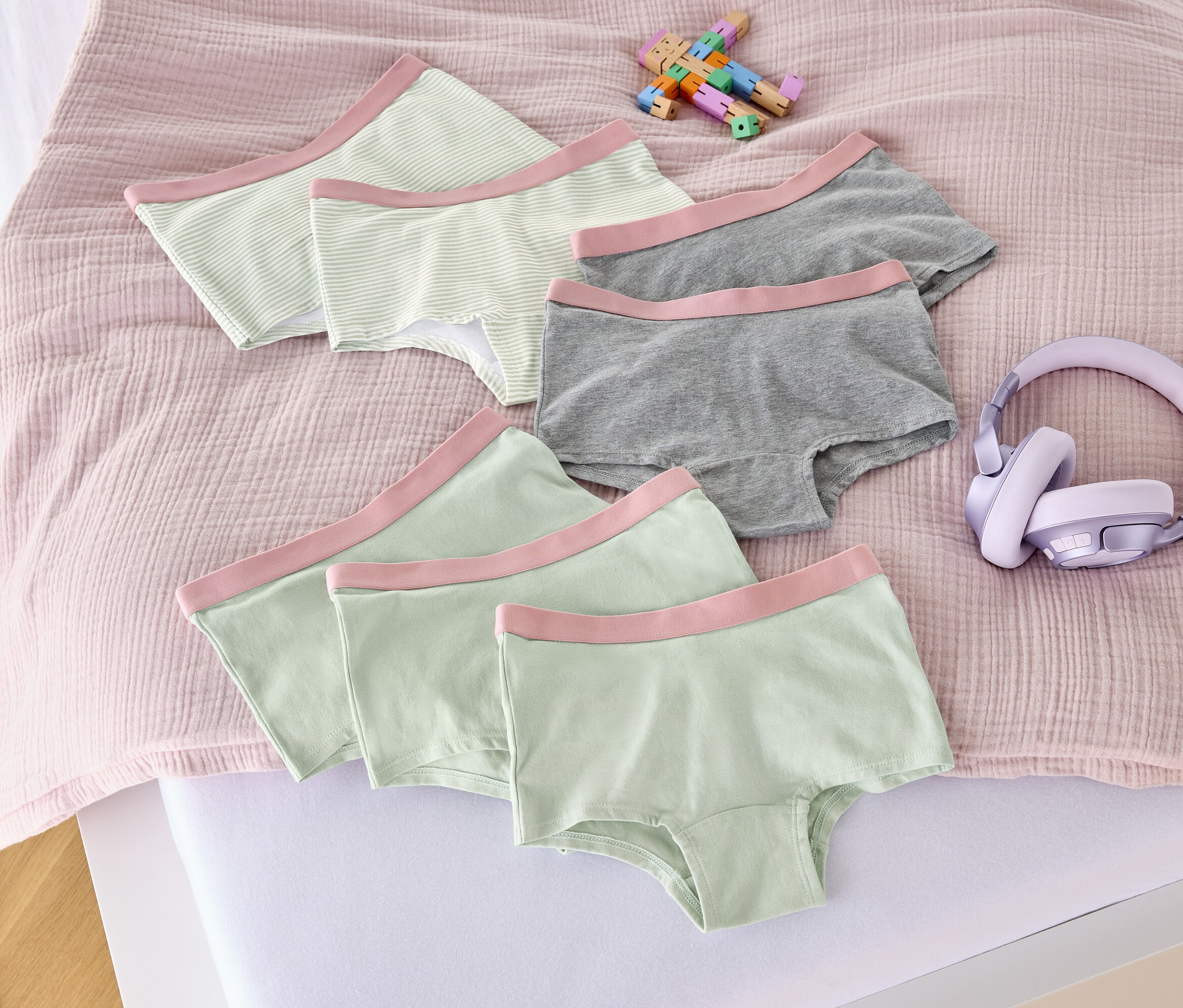 Egy ágyon hét rózsaszín kislány bugyi, egy játék és egy fejhallgató található.