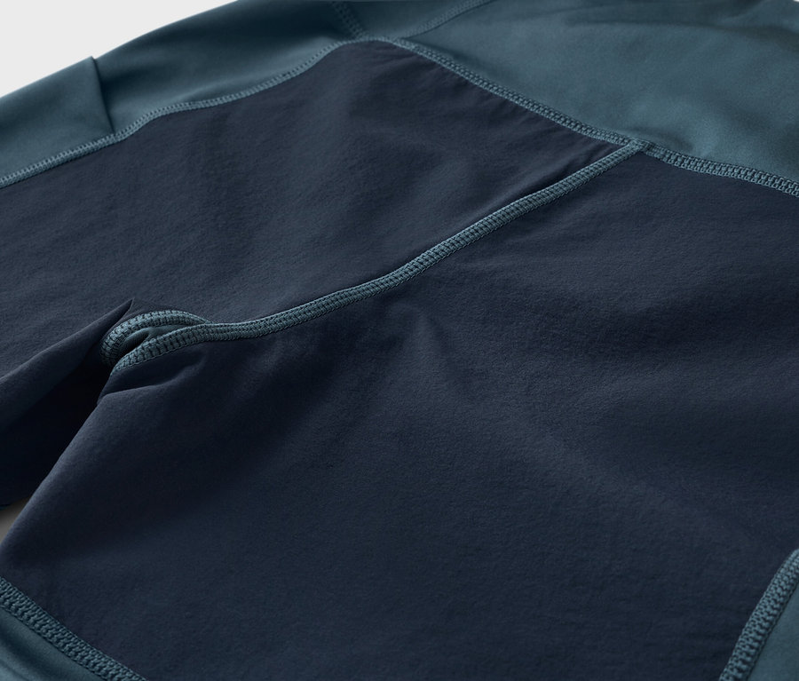 Egy sötétkék-zöld nadrág közeli képe sötétebb, négyzet alakú betétekkel.