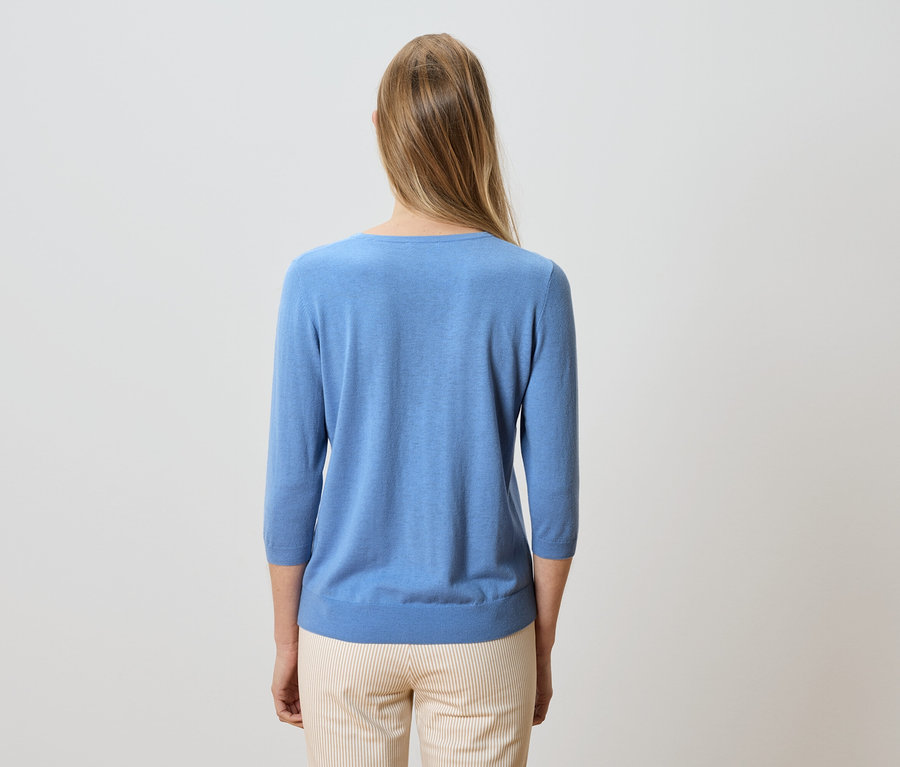Hátulnézet egy szőke, hosszú hajú nőről, aki világoskék pulóvert és csíkos nadrágot visel.