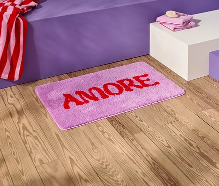 A fa padlón egy lila fürdőszobai szőnyeg piros "AMORE" felirattal.