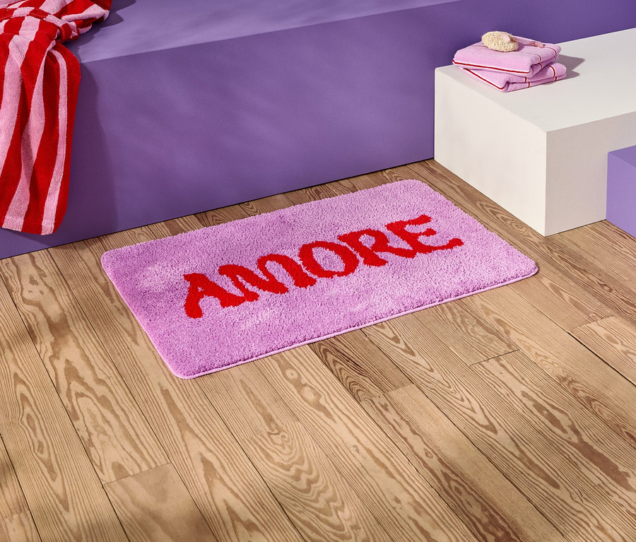 A fa padlón egy lila fürdőszobai szőnyeg piros "AMORE" felirattal.