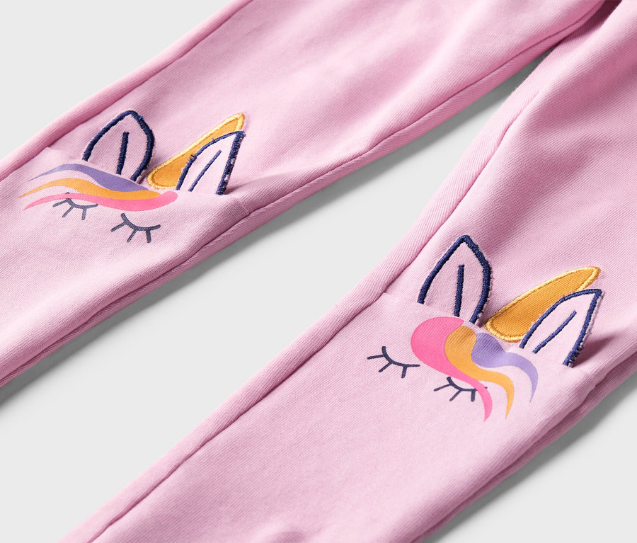 Rózsaszín leggings közeli képe, a térdén hímzett unikornis arcokkal.