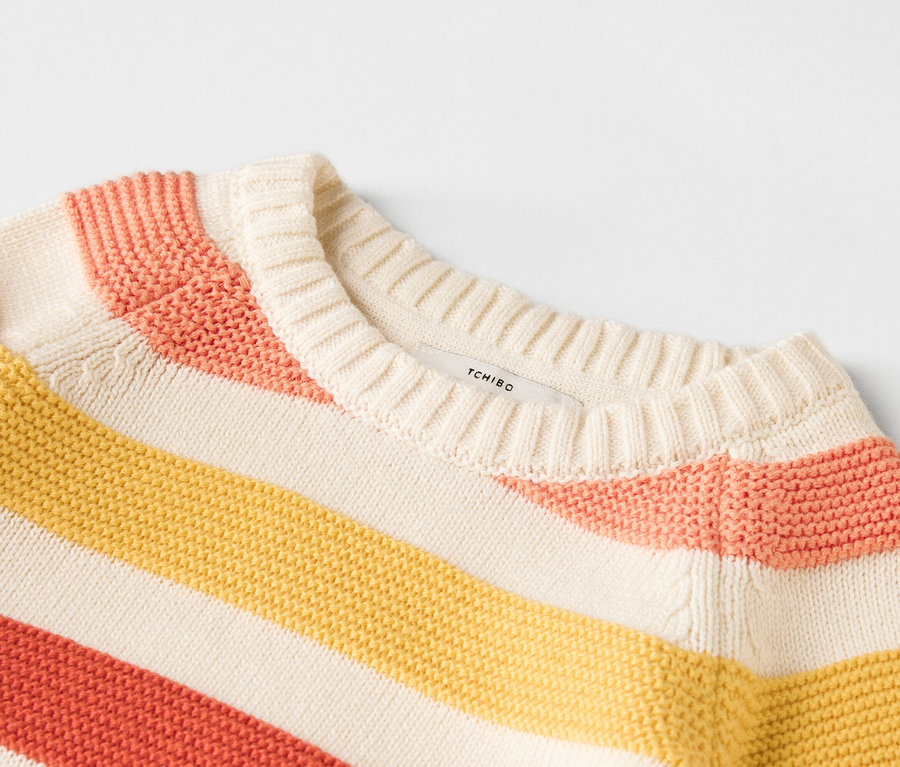 Közeli kép egy sárga, rózsaszín és bézs csíkos pulóverről.