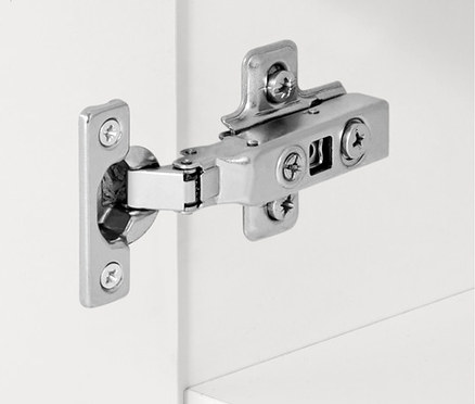 Ezüst színű zsanér részlete egy fehér szekrényen.