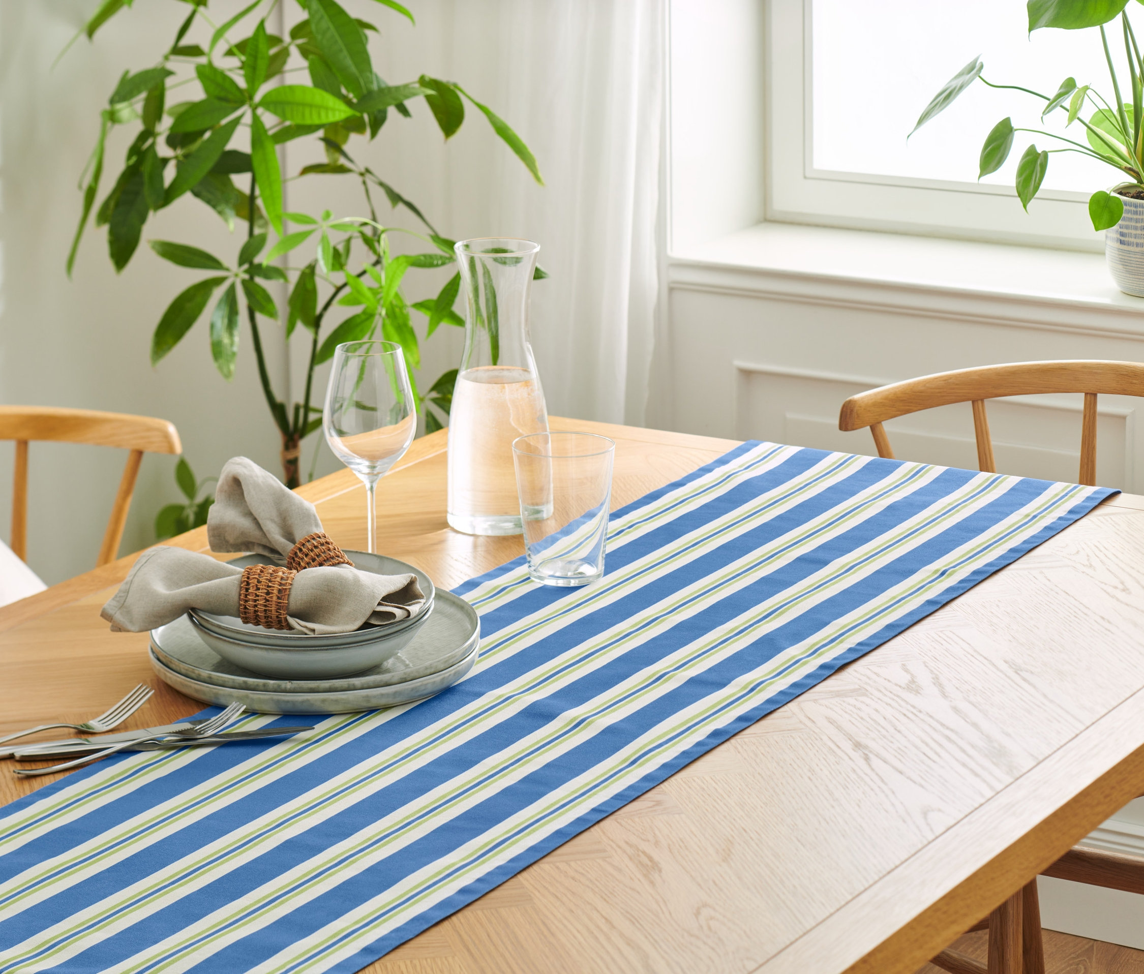 Terített asztal pamut asztali futóval, csíkos, tányérokkal, poharakkal és vászon szalvétákkal.