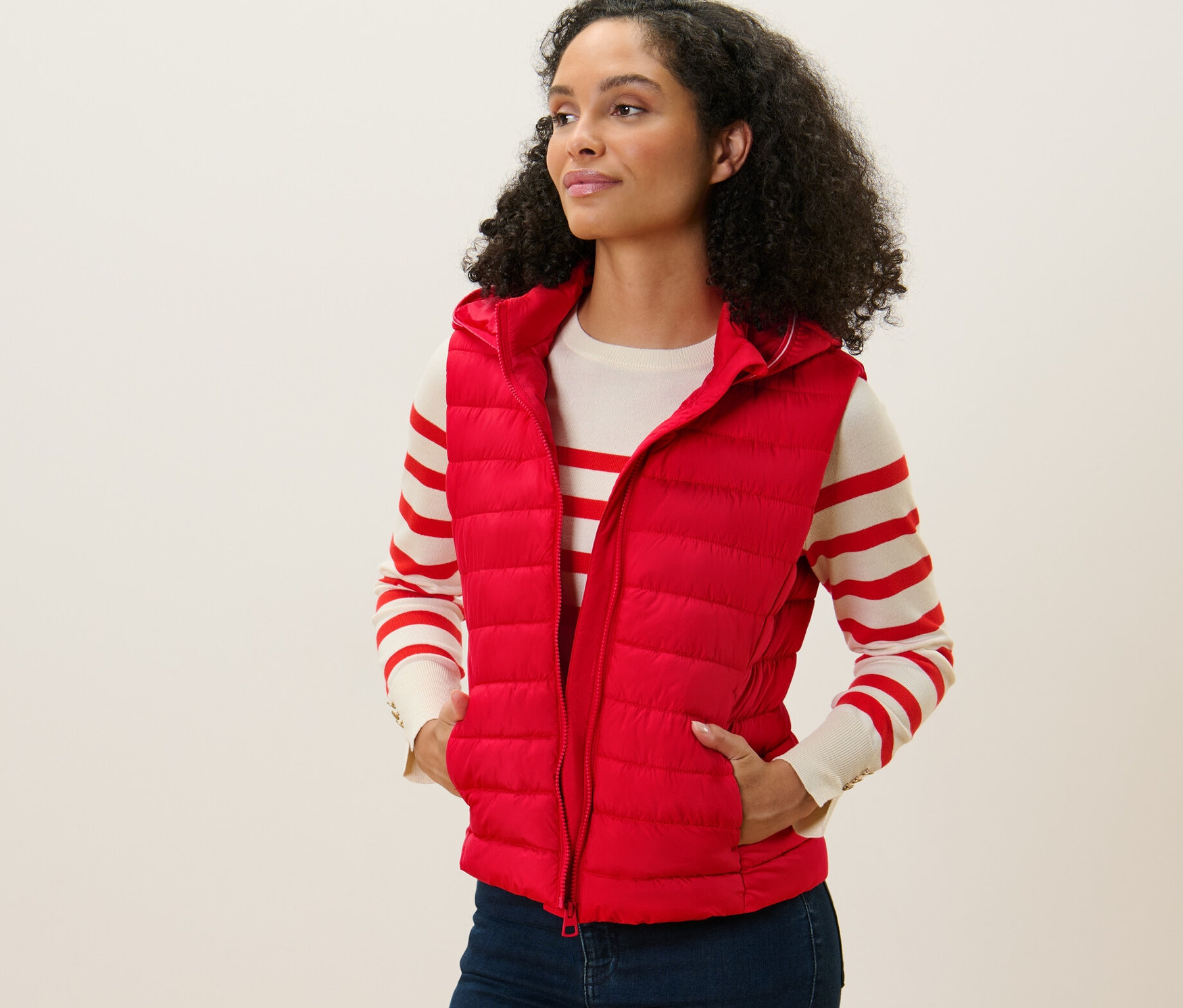 Nő visel piros, kapucnis, steppelt mellényt, áll és balra néz.