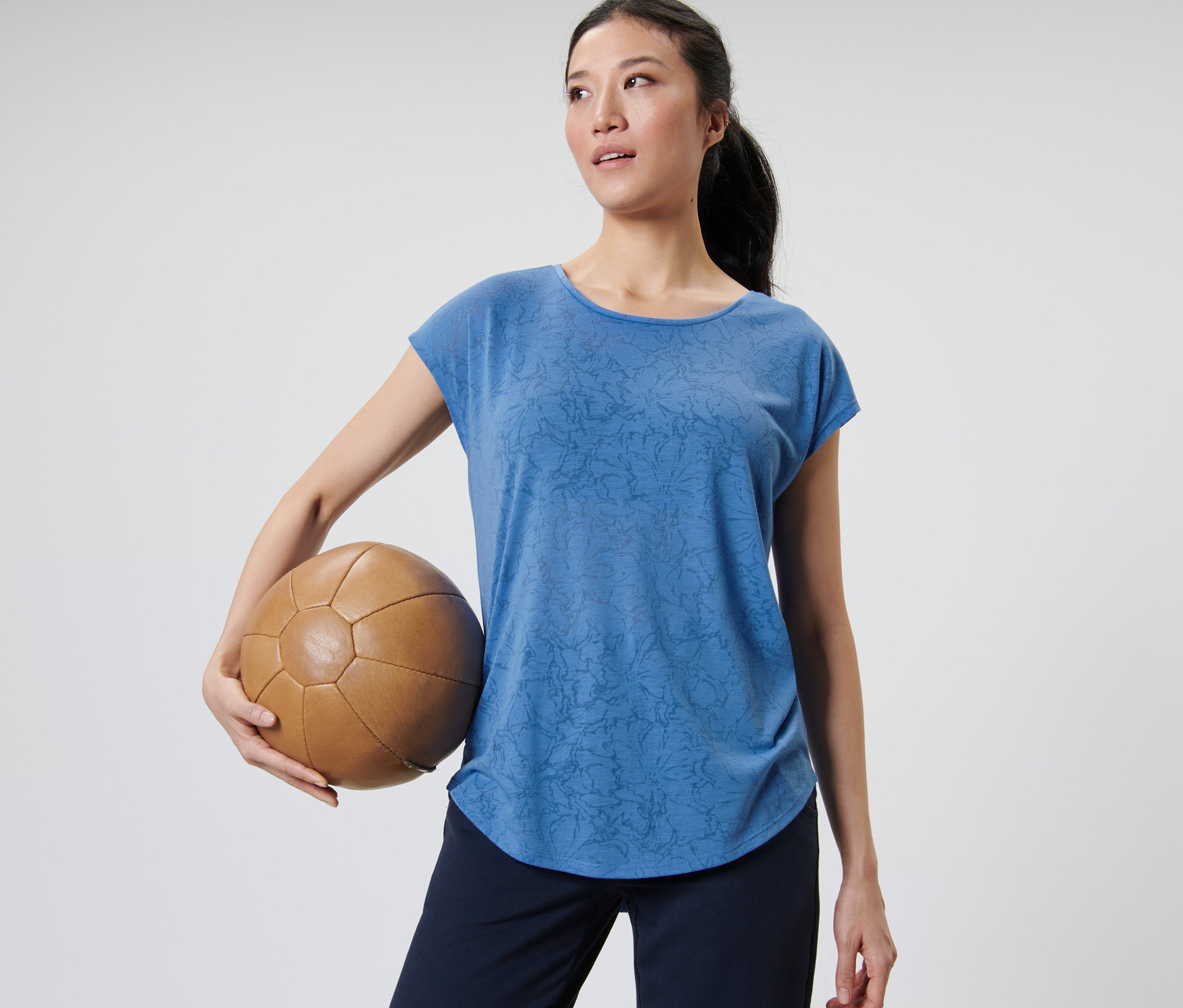 Nő tart egy barna bőr labdát és kék sportfelsőt visel.
