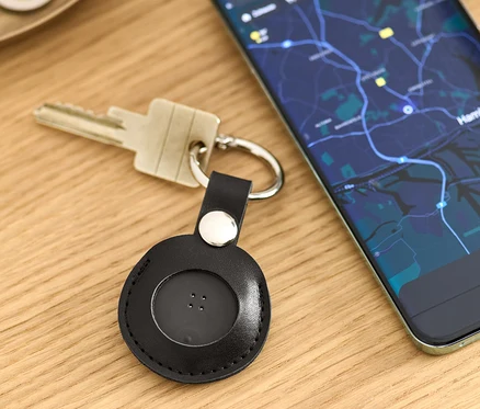 Az asztalon kulcsok fekszenek egy fekete okos nyomkövető akasztóval és egy térképet mutató mobiltelefon mellett.
