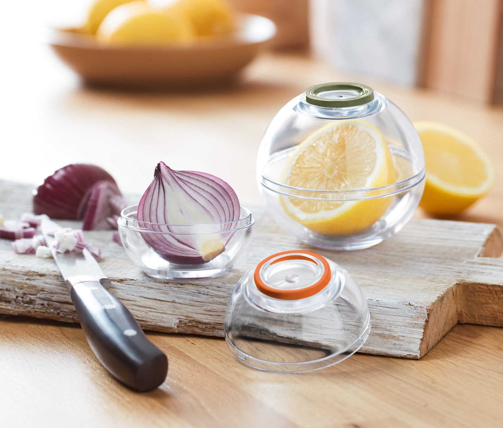 Fél hagyma egy 2 frissentartó gömbben és fél citrom egy 2 frissentartó gömbben egy vágódeszkán.