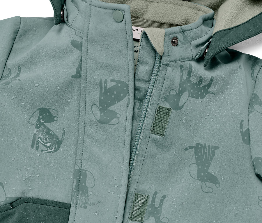Egy zöld, esőben színváltó, kutyás és csizmás mintájú gyerek softshell kabát részlete, vízcseppekkel.
