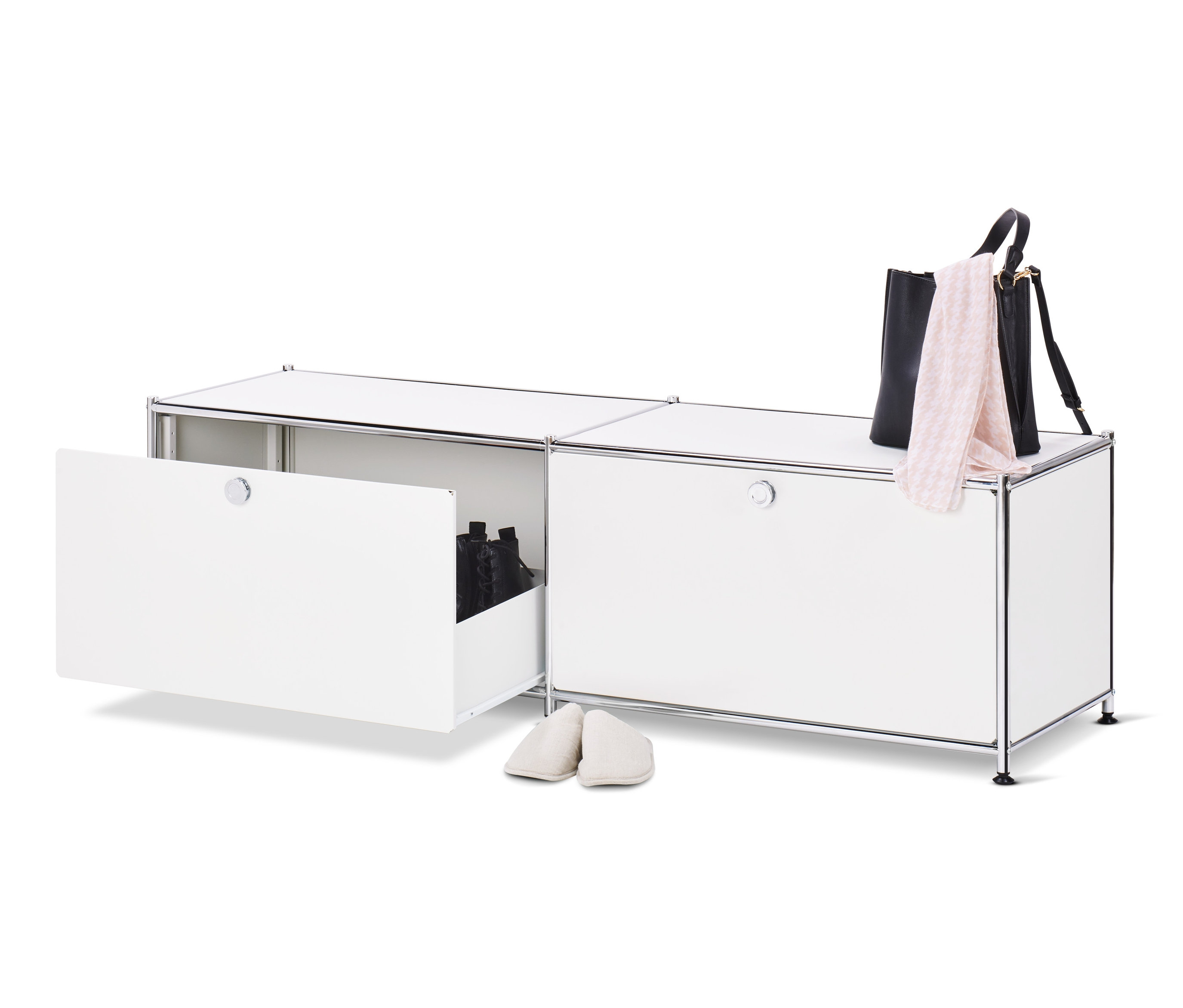 Egy nyitott fehér »CN3« alacsony komód fiókokkal és cipőkkel belül, mellette egy pár krémszínű papucs, a komód tetején egy fekete kézitáska és egy rózsaszín kendő.