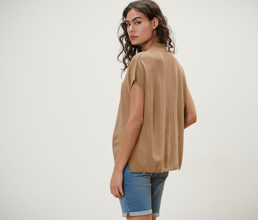 Nő néz a válla fölött, rövid ujjú, bézs kardigánt visel.