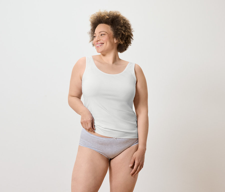 Egy mosolygó, afro frizurás nő fehér trikót és csíkos alsóneműt visel.
