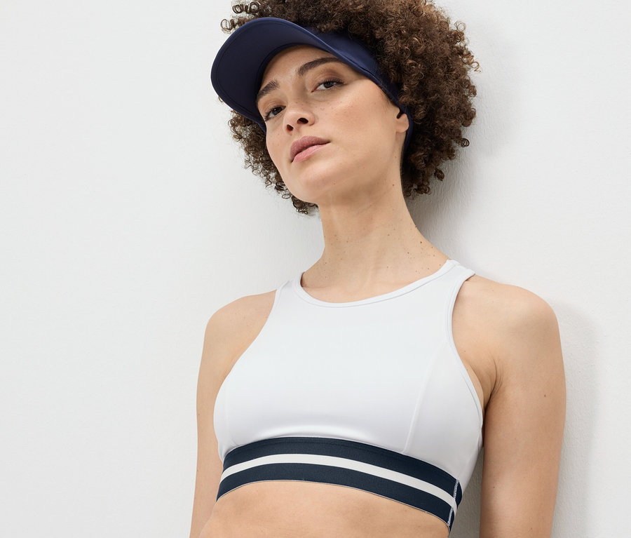 Nő visel egy fehér »Crop Top« sportmelltartót és egy kék napellenzőt.