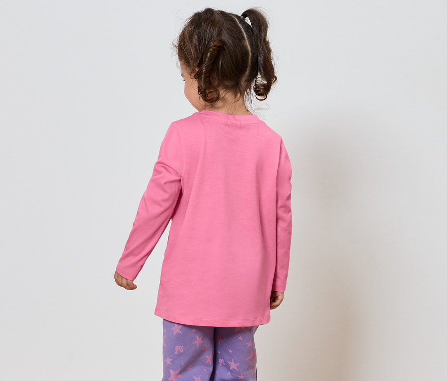 Egy kislány barna hajjal, rózsaszín hosszú ujjú pólóban és lila, csillagmintás nadrágban áll háttal a nézőnek.