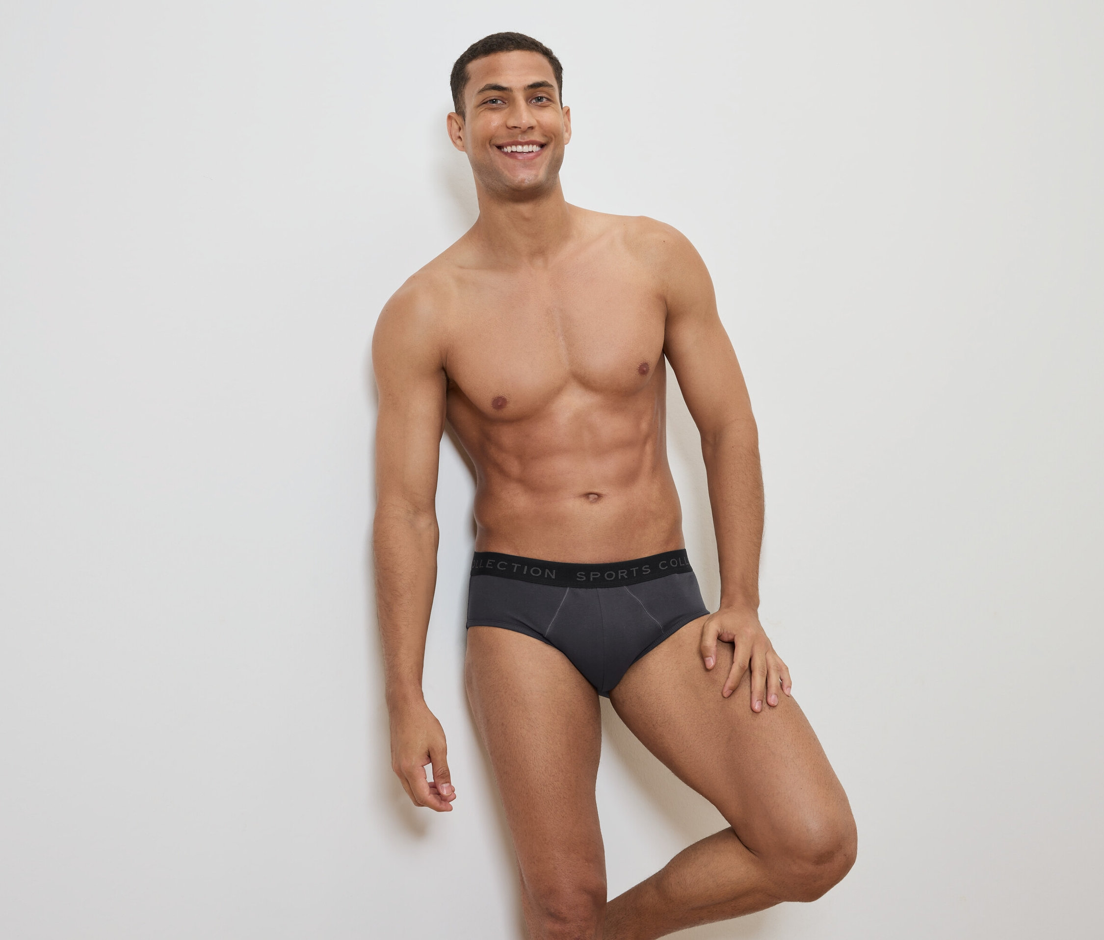 Mosolygó, felsőtestét szabadon hagyó férfi szürke alsónadrágban, fekete derékpánttal pózol.