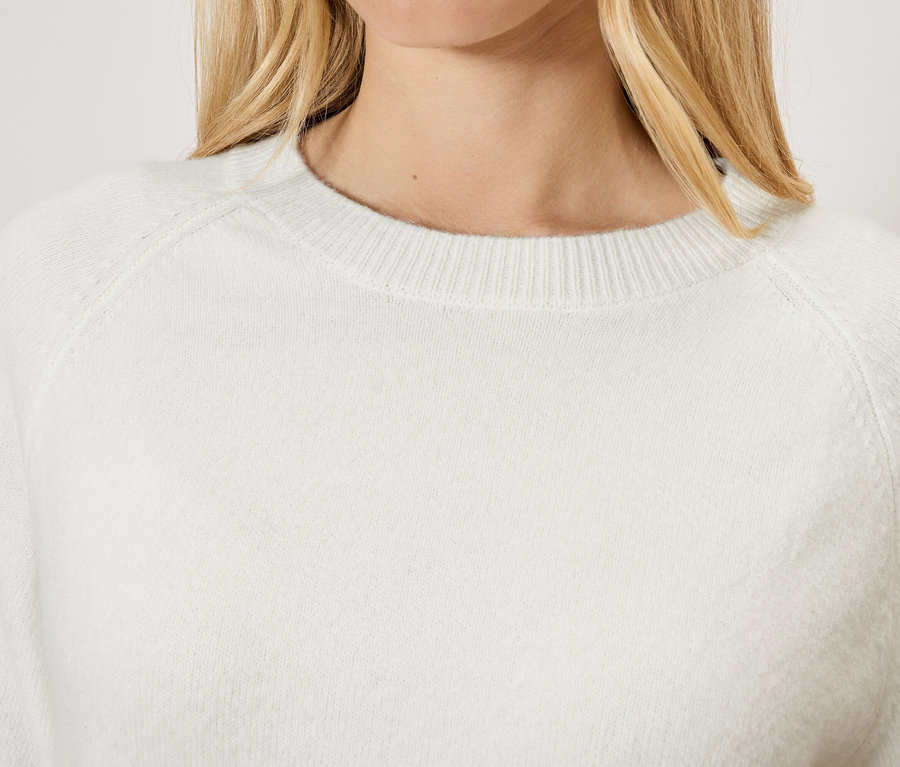 Szőke hajú nő fehér pulóvert visel.