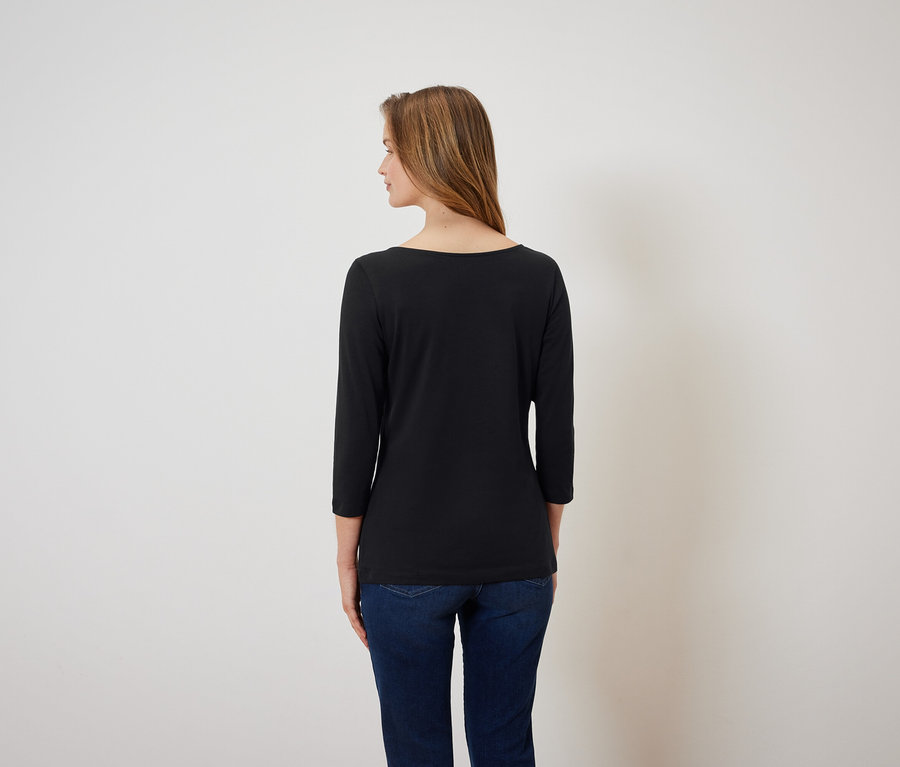 Egy hátulról látható, barna hajú nő fekete, háromnegyedes ujjú pólót és kék farmert visel.