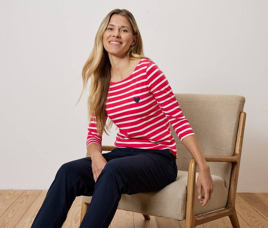 Egy nő egy széken ül, piros-fehér csíkos pólót és sötétkék nadrágot visel.