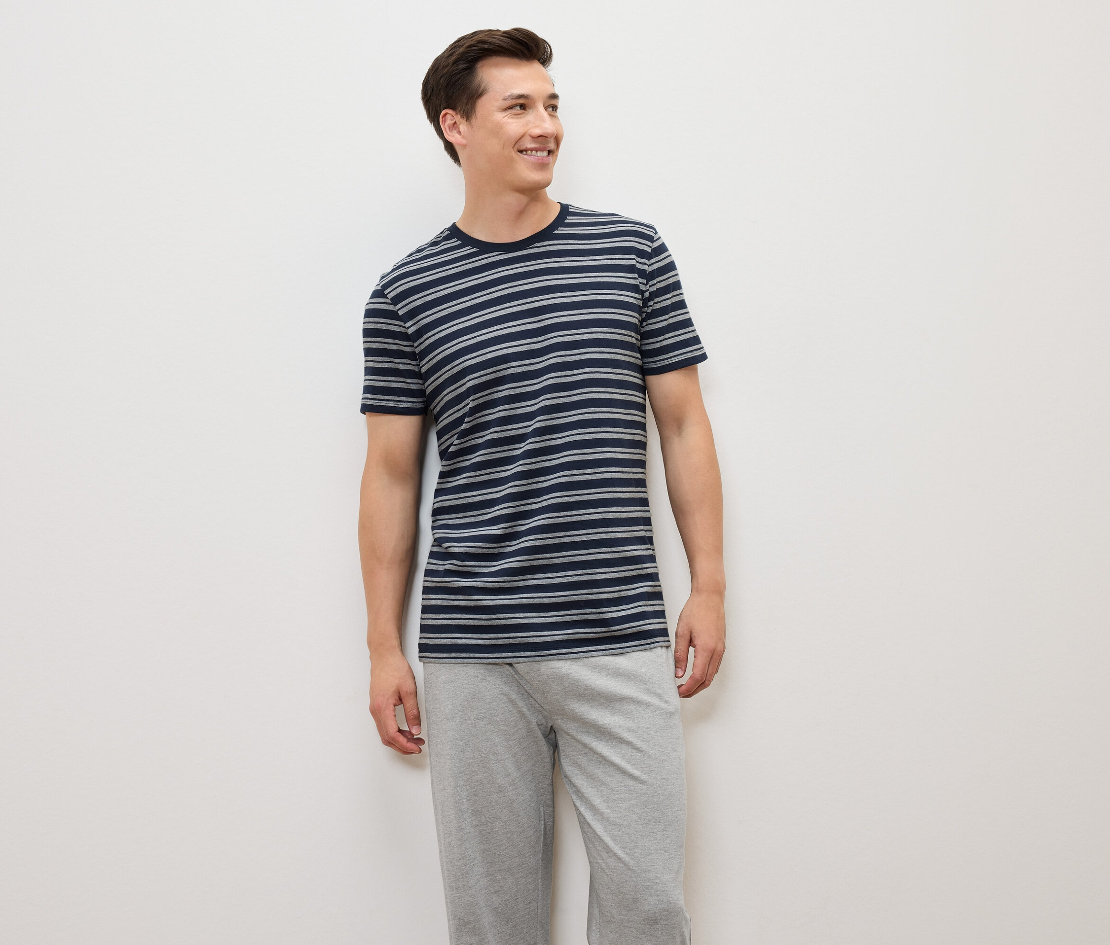 Egy férfi áll, kék-szürke csíkos pólót és szürke nadrágot visel.