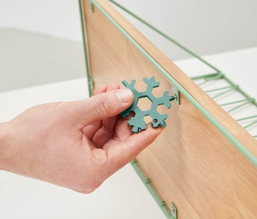 Egy kéz egy multifunkciós kulcsot tart, és meghúz egy csavart egy fa polcon.