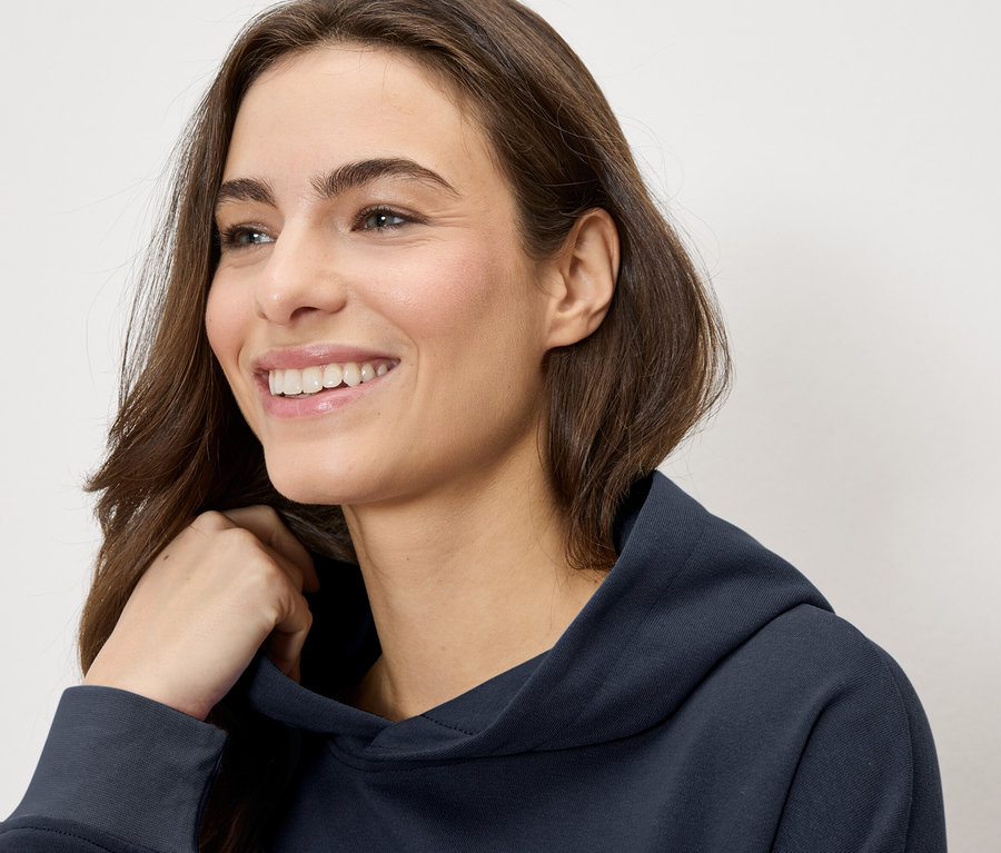 Mosolygó nő tengerészkék kapucnis pulóverben.