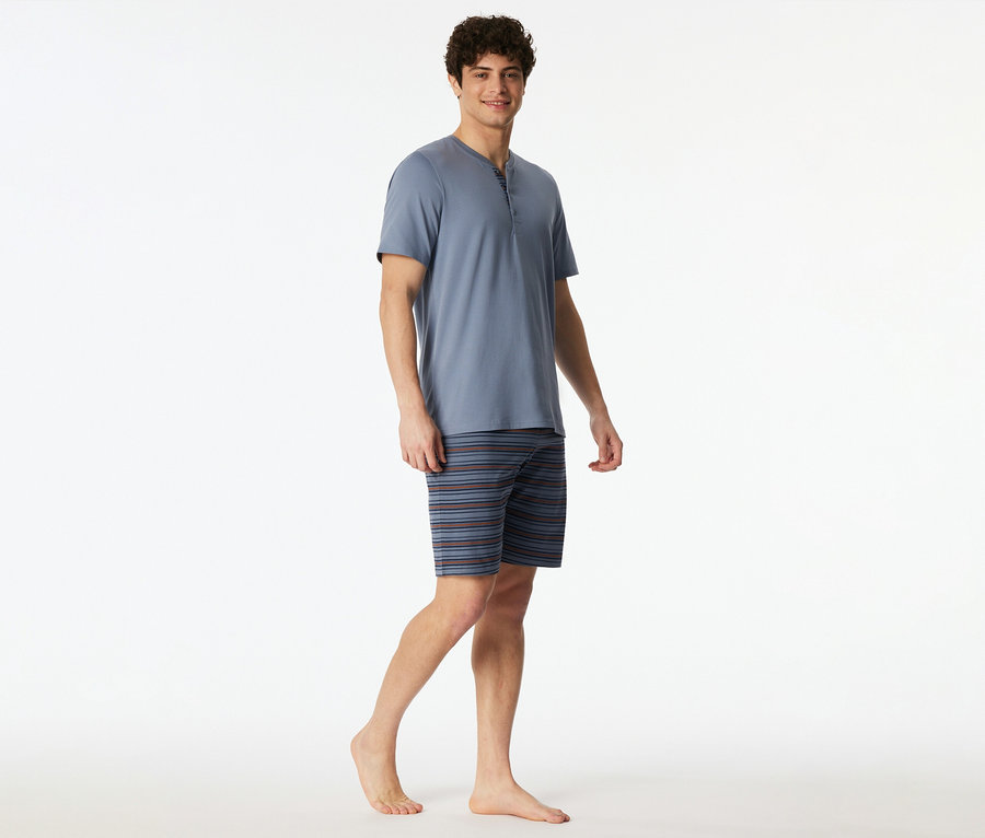 Férfi visel kék pólóból és csíkos rövidnadrágból álló pizsamát.