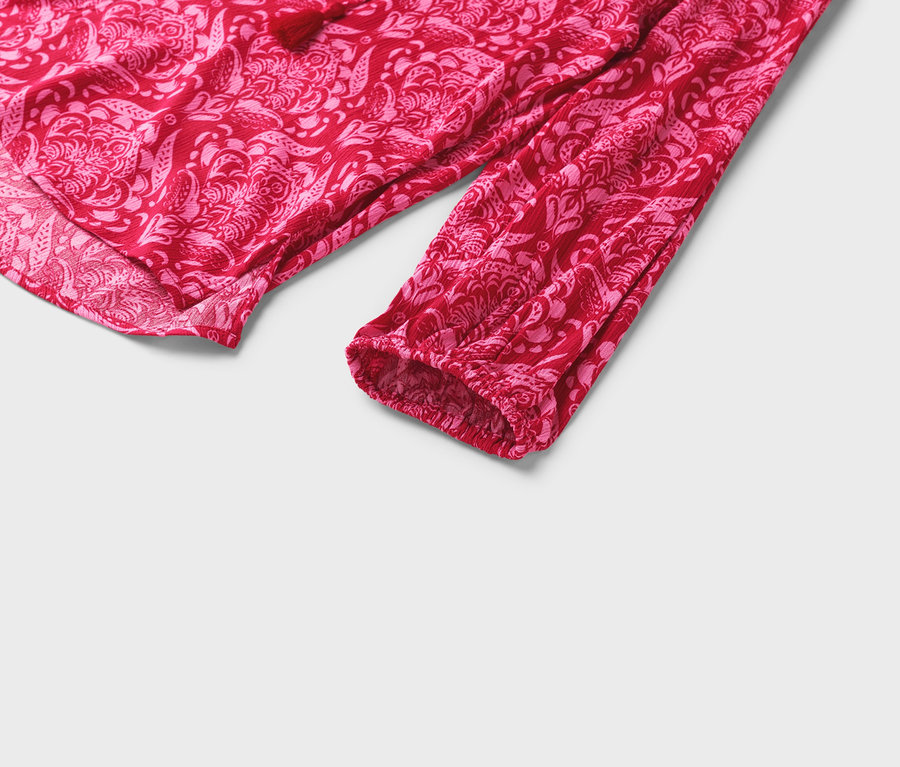 Egy piros blúz részletgazdag képe rózsaszín virágmintával és hosszú ujjakkal.