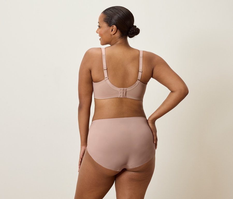 Egy hátulról látható nő testszínű melltartót és bugyit visel, egyik kezét a csípőjén tartja.