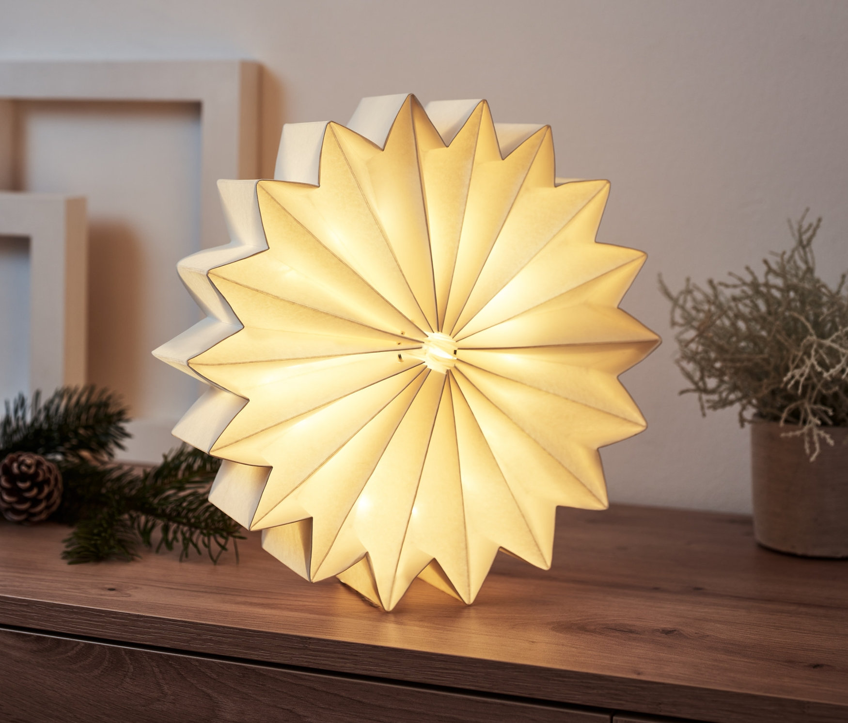 Egy fa komódon világító LED-es csillag áll. A háttérben képkeretek és karácsonyi dekoráció látható.