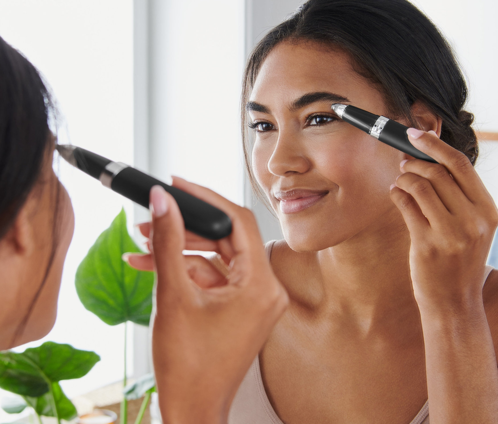 Nő formázza a szemöldökét elektromos szemöldökformázóval a tükör előtt.