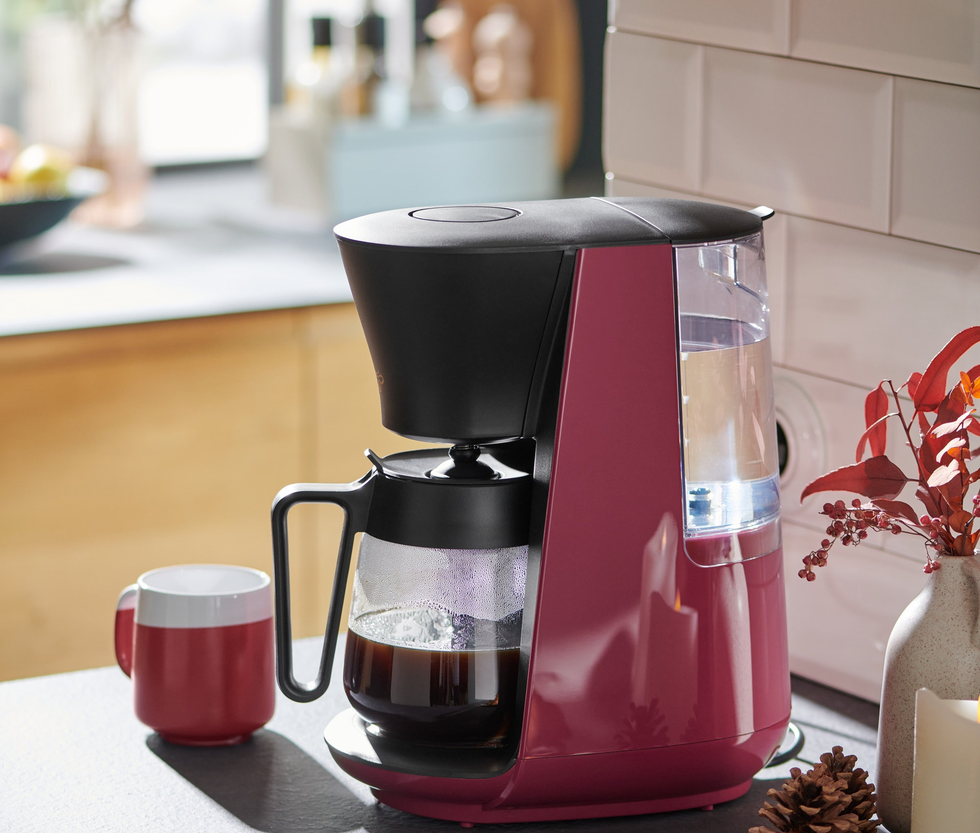 A berry színű »Let's Brew« filteres kávéfőző egy piros kávésbögre mellett áll a konyhapulton.