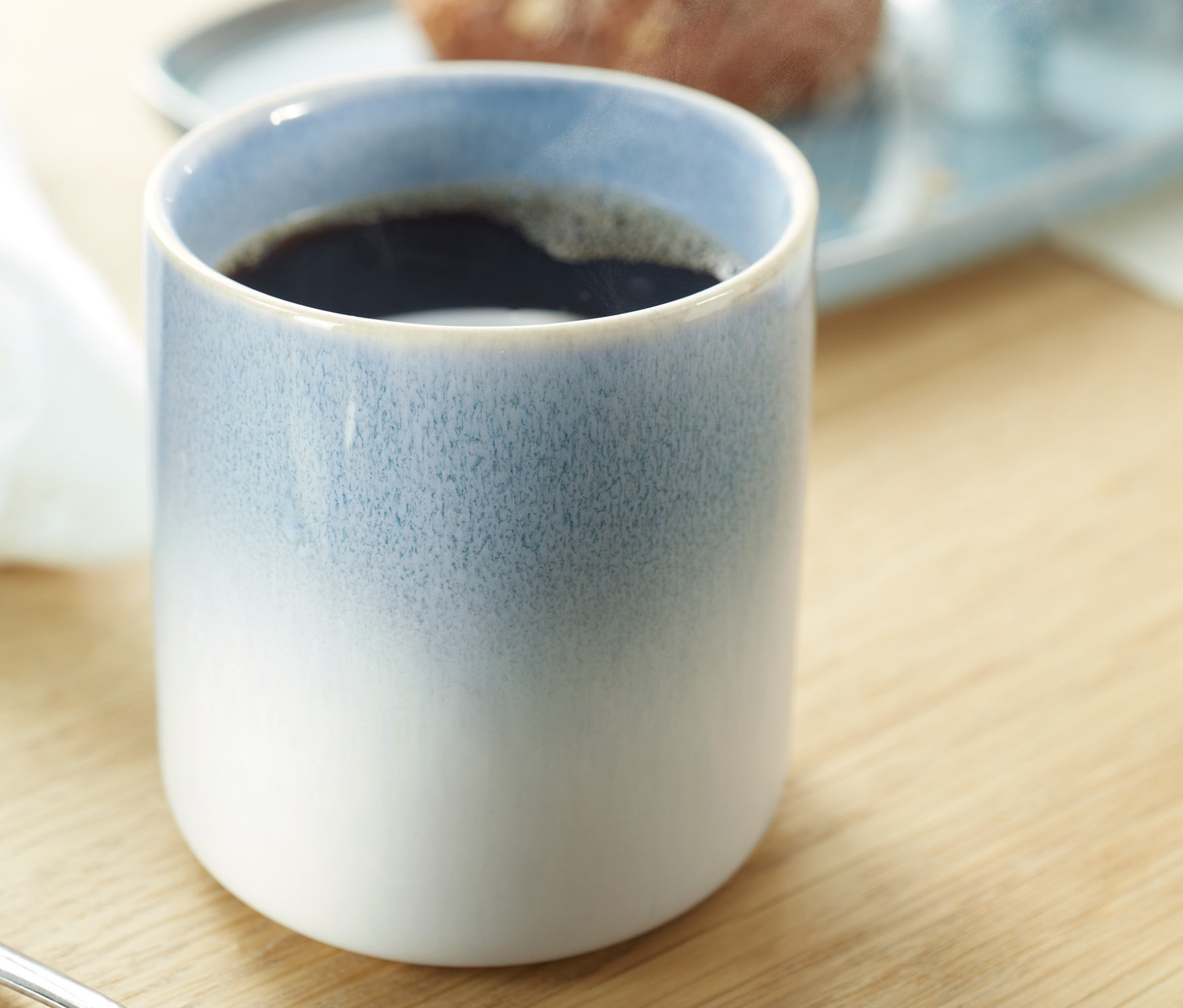 Kávésbögre közeli felvétele. A háttérben egy tányér étel látható.