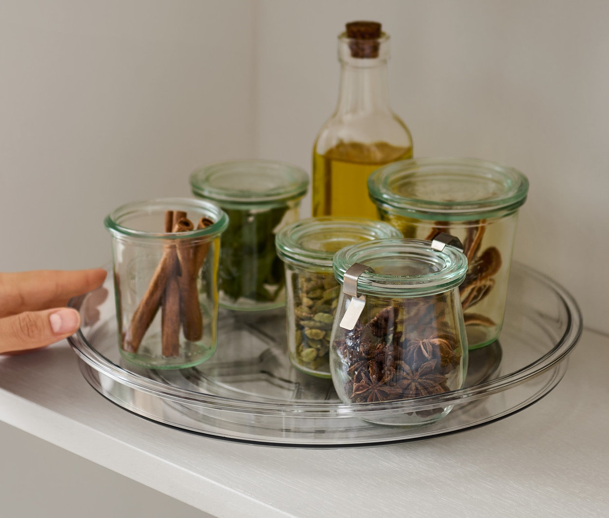 Egy kéz nyúl egy fűszerekkel teli forgótálcához a polcon.