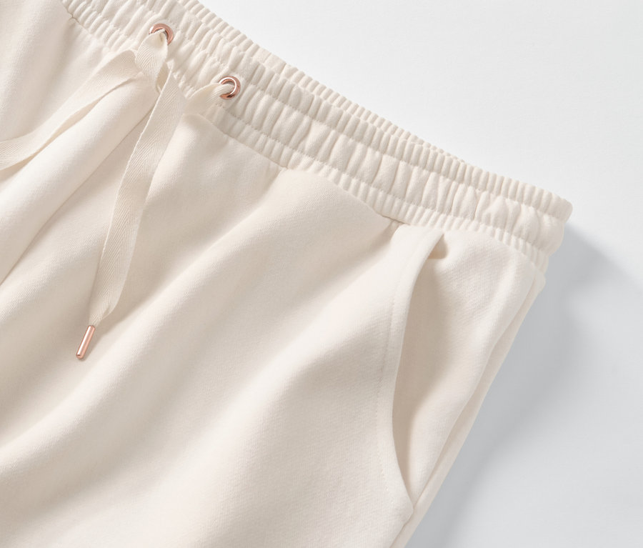 A krémszínű női szabadidő szett alsó részletének ábrázolása, elasztikus derékpánttal és húzózsinórral.