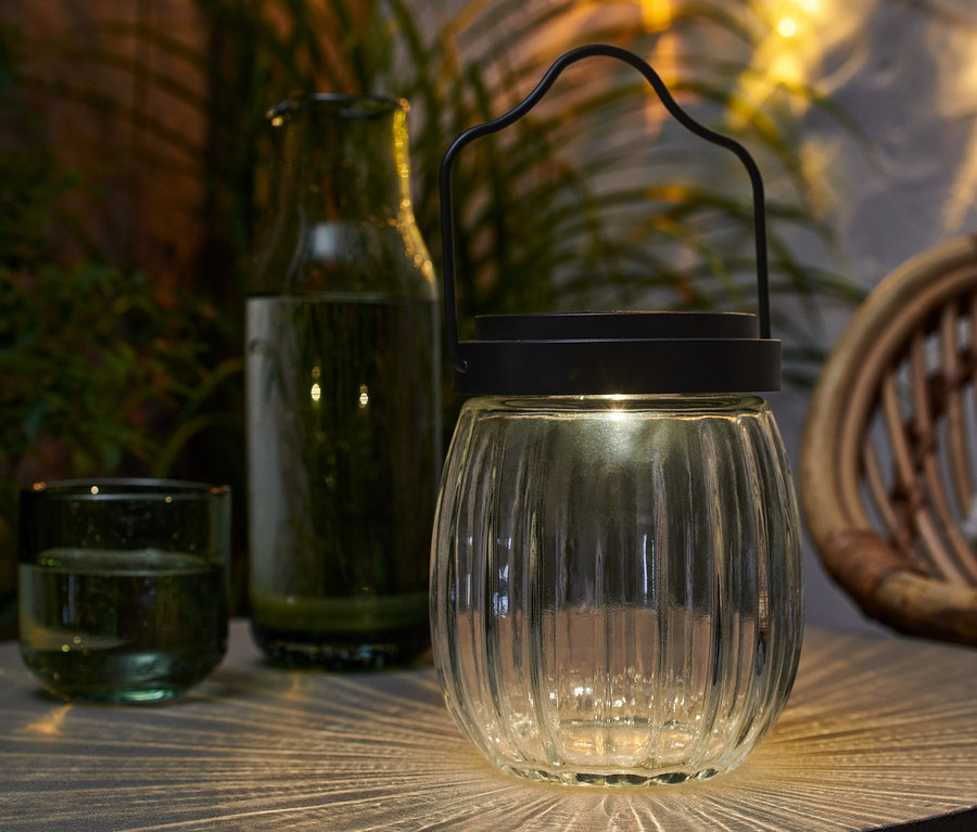 Egy üveg napelemes lámpa áll az asztalon egy pohár és egy üveg mellett.